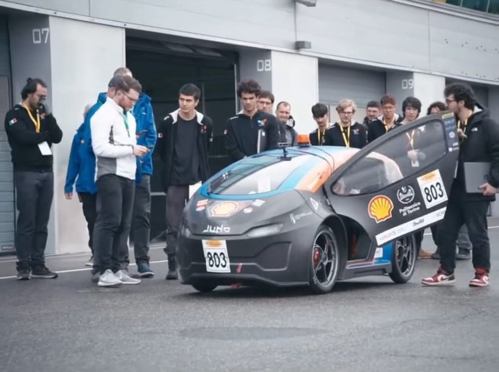 The team standing around Juno, number 803, in the Shell Eco-marathon paddock